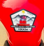 Hikkim 14,570 FT post office sticker stuck onto a red motorcycle fuel tank.